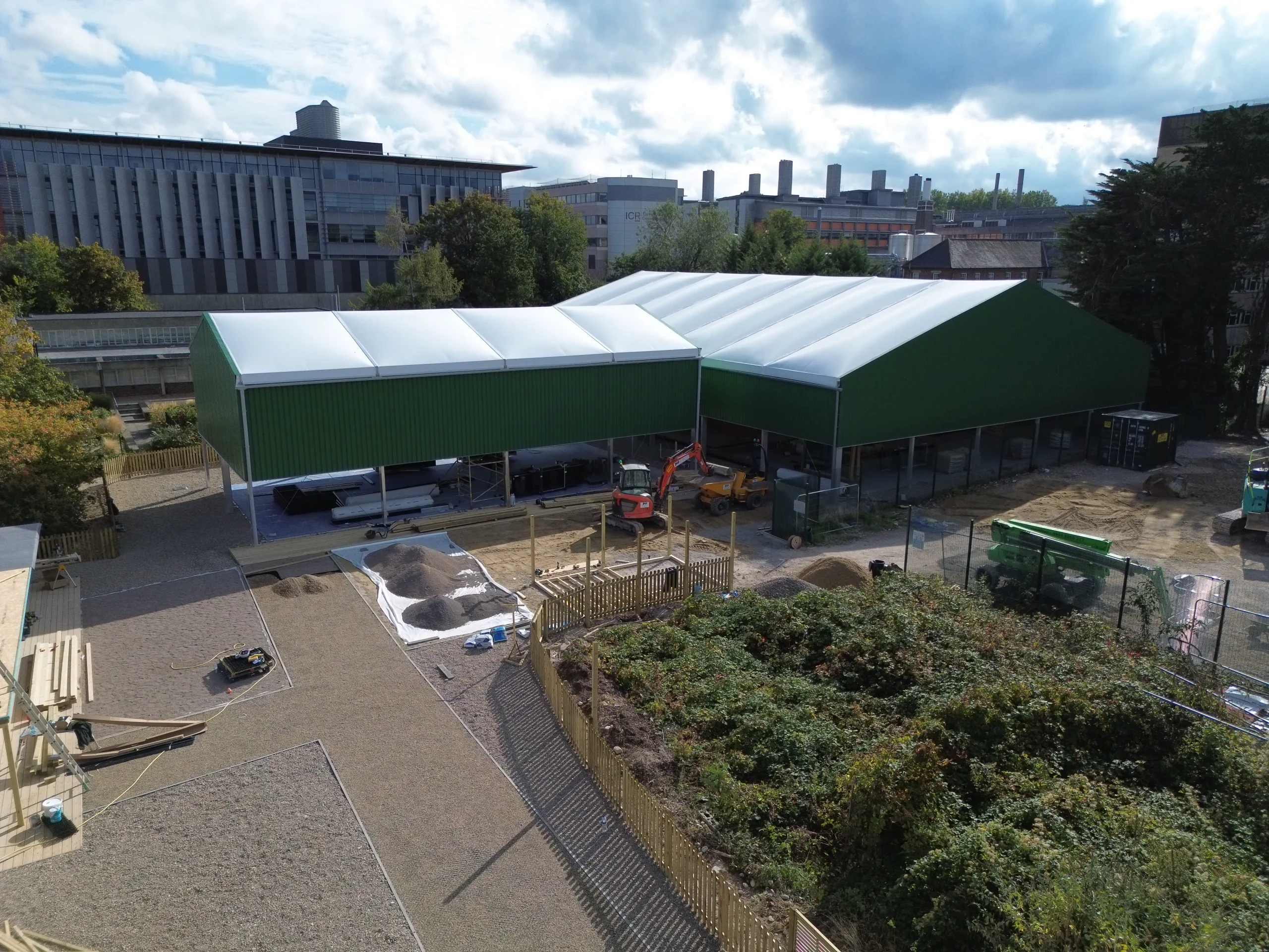 Construction site of a new four-court covered padel facility in Sutton, featuring green buildings, construction machinery, and landscaped areas.