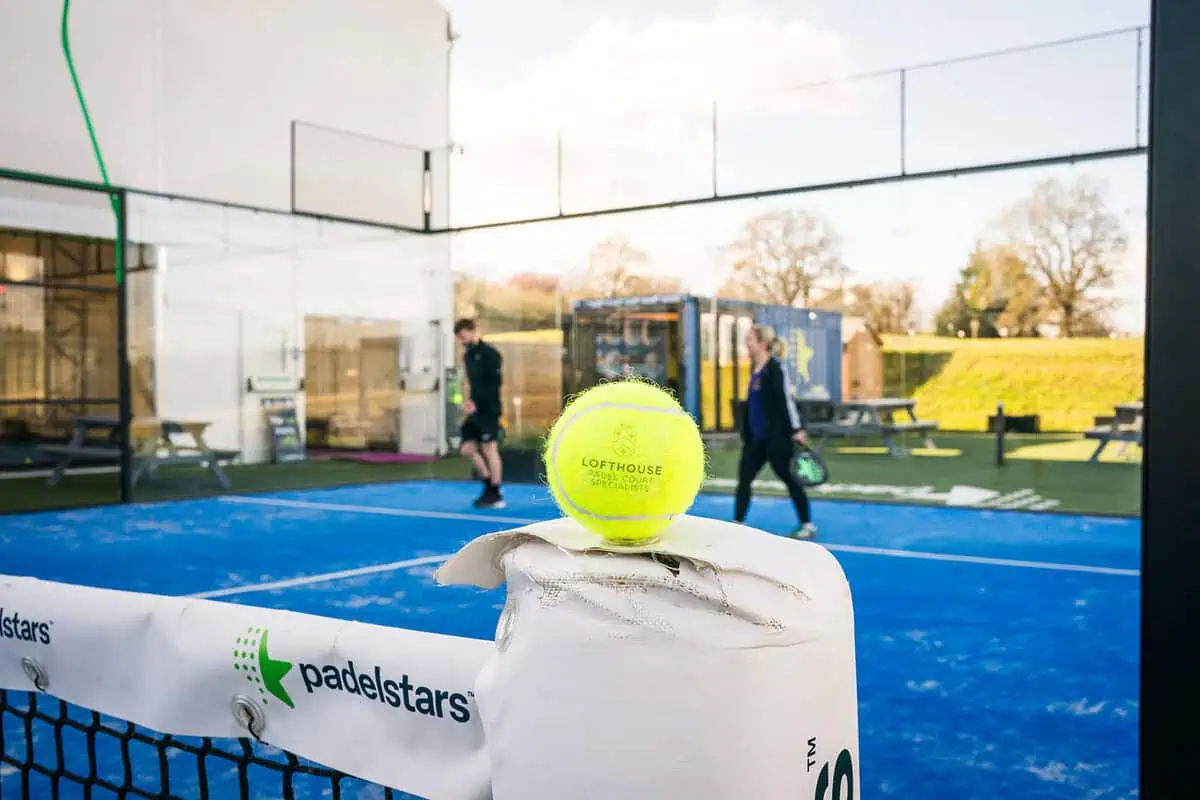 Padel ball on net at Lofthouse padel court, with players in background, illustrating differences between padel and tennis balls.