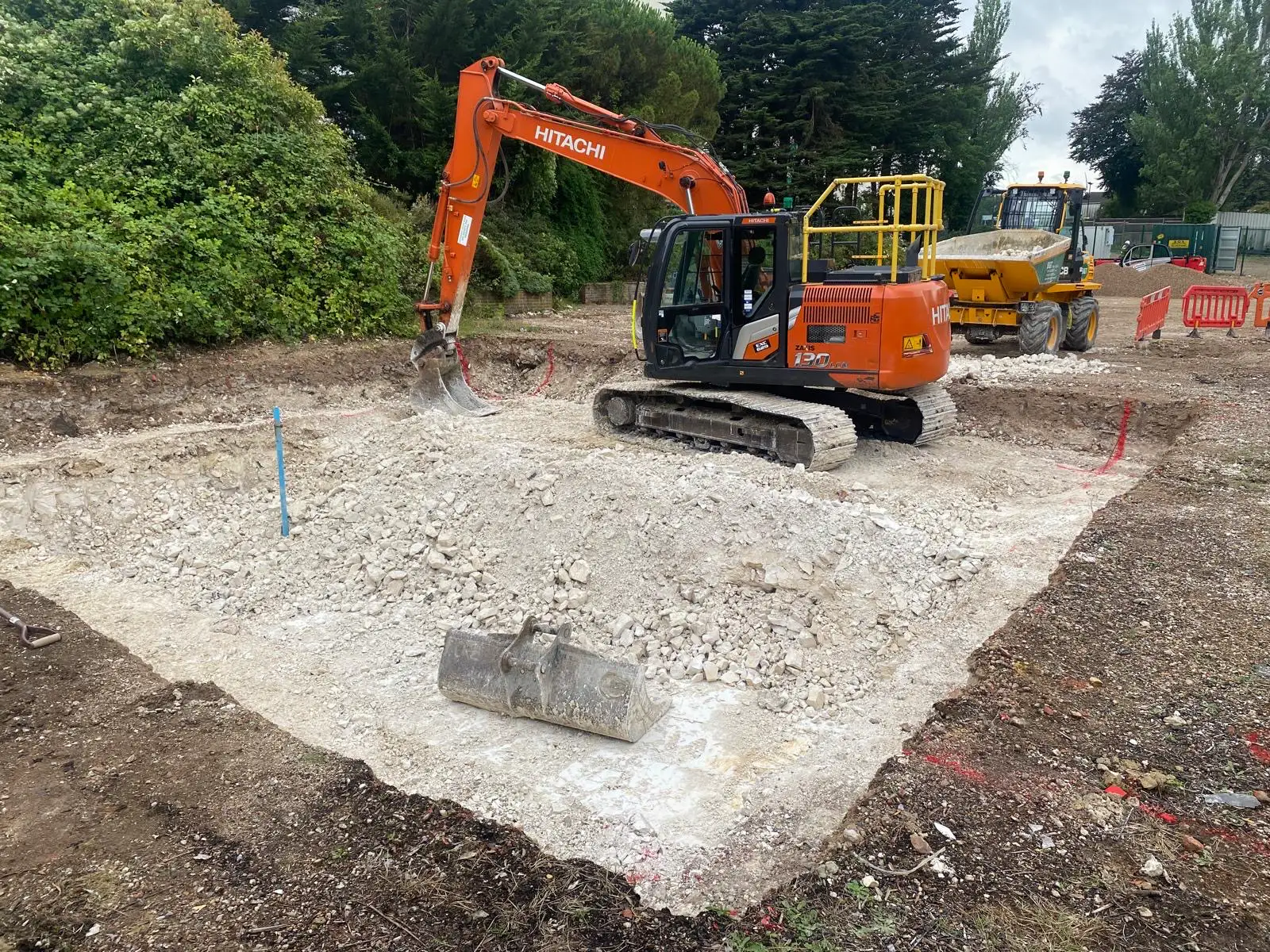 Excavator working on site preparation for new padel courts at Social Sports Society in Sutton, with construction materials and machinery visible.