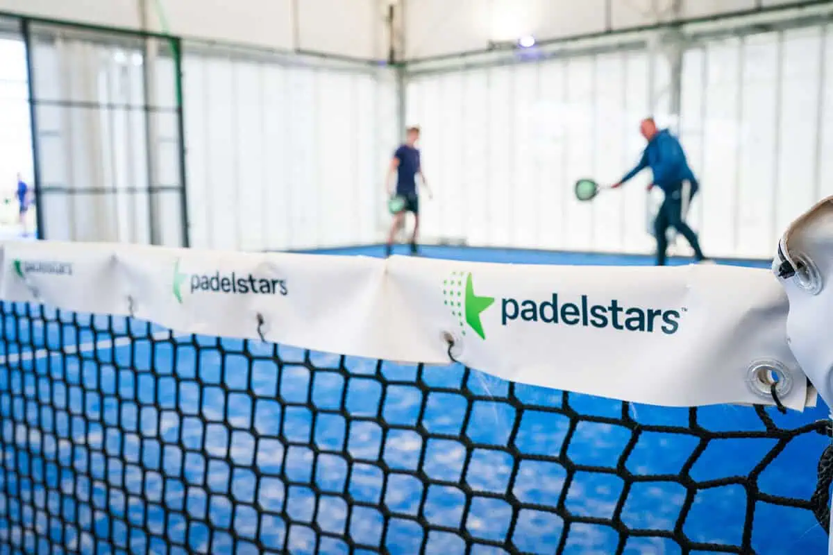 Padel court with players in action, featuring a branded net with "padelstars" logo, highlighting the sport's social aspect and professional installation.
