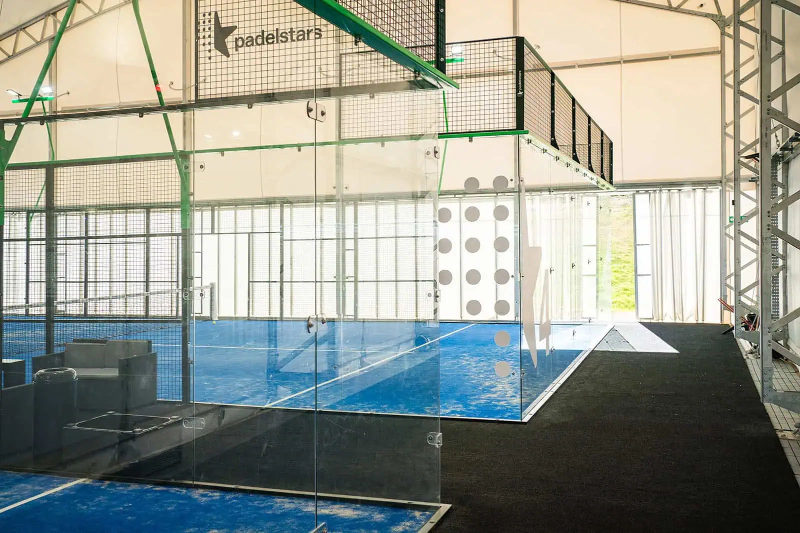 Indoor padel court interior featuring glass walls, artificial lighting, and blue playing surface, illustrating specialist design elements for optimal visibility and player comfort.