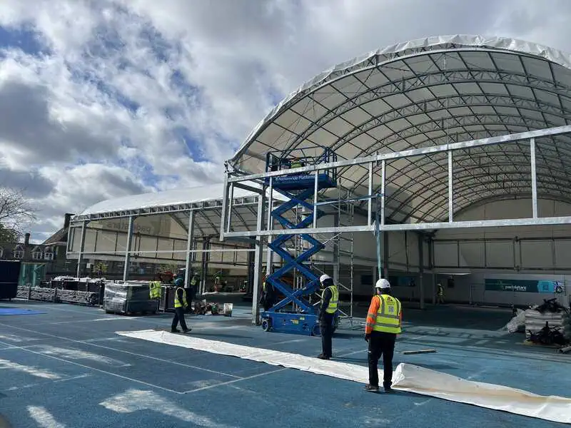 Construction site of covered padel courts at Batchwood Golf & Sports Centre, workers in safety gear, scissor lift, blue court surface, showcasing installation progress and modern design.