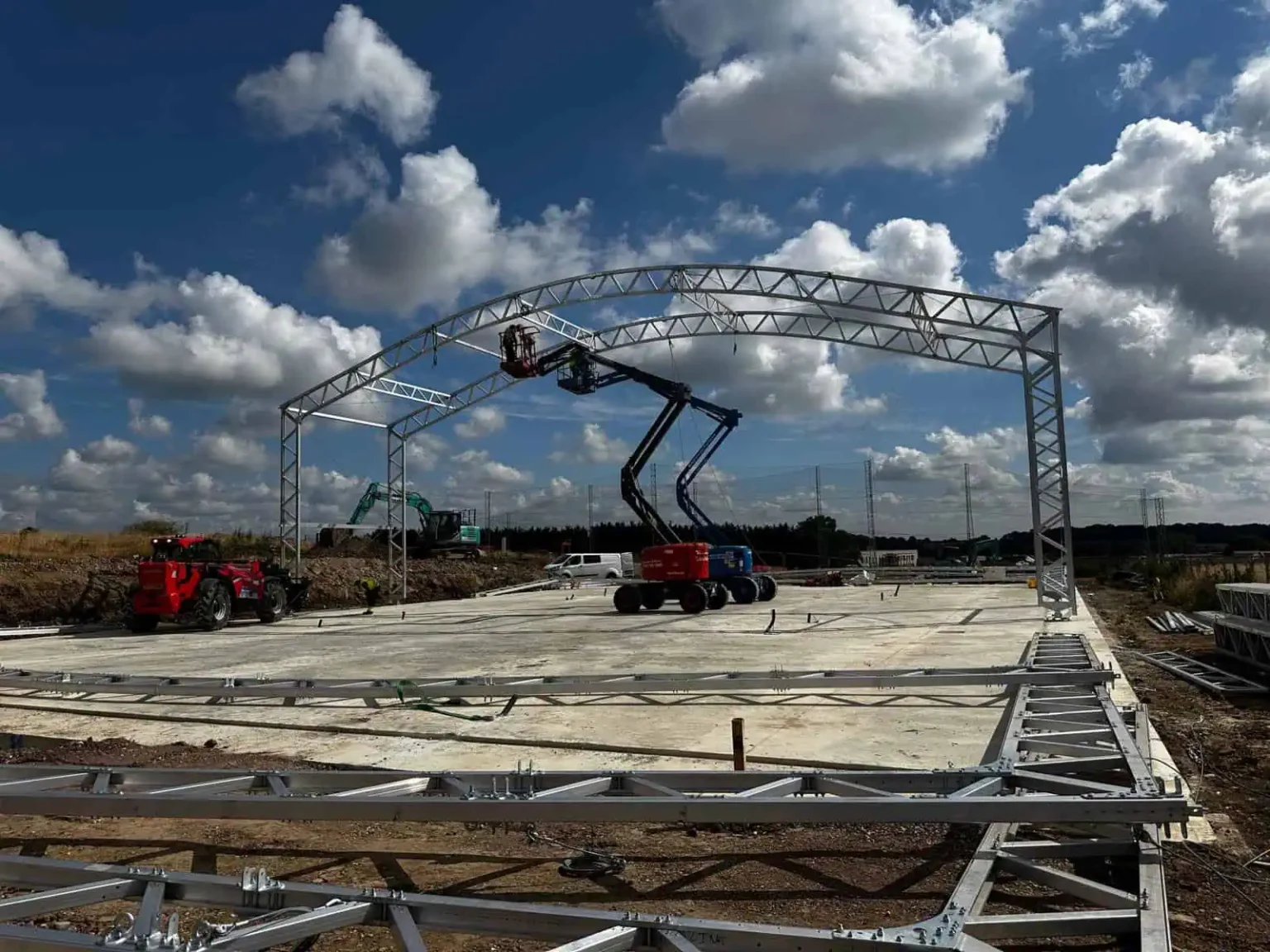 Construction site for a padel court in Southampton, featuring a large metal frame being installed with machinery, under a partly cloudy sky, emphasizing the progress of bespoke court construction.